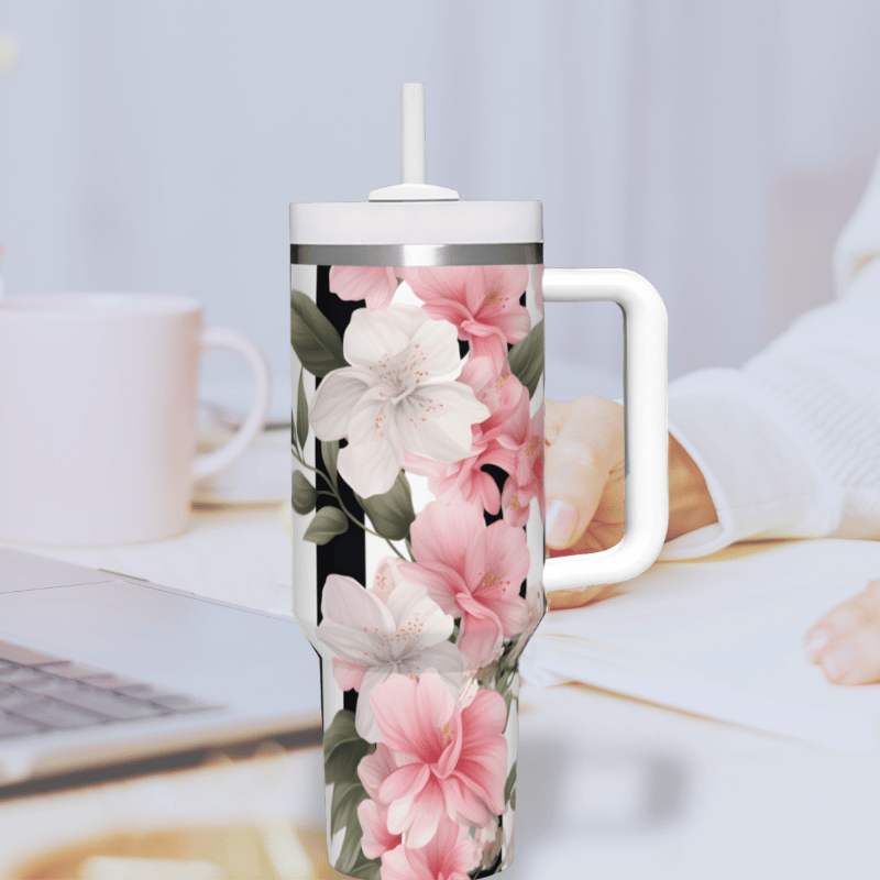 a coffee mug with pink flowers on it next to a laptop