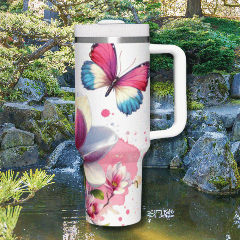 a white and pink butterfly travel mug next to a pond of water